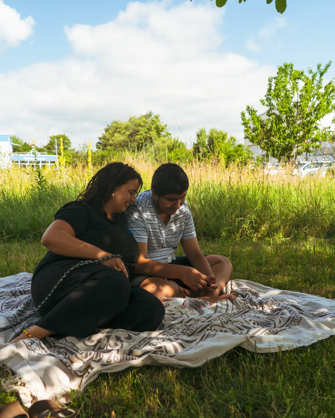 Eine Mitarbeiterin von ABW Stütz Punkt sitzt mit einem jungen Mann auf einer Wiese und unterhält sich mit ihm